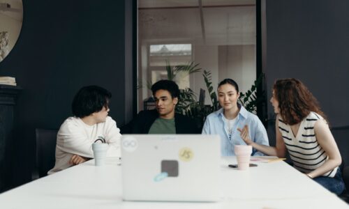 A diverse group of four young clinicians seated around a conference table engaged in collaborative discussion during a group supervision session.